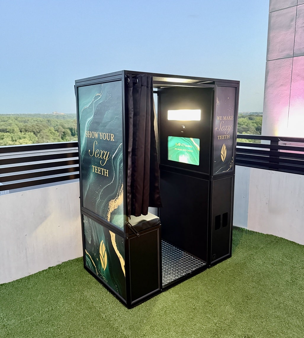 Photo booth on a rooftop terrace with teal panels and the words 'Show Your Sexy Teeth' along the side, curtain open for use.