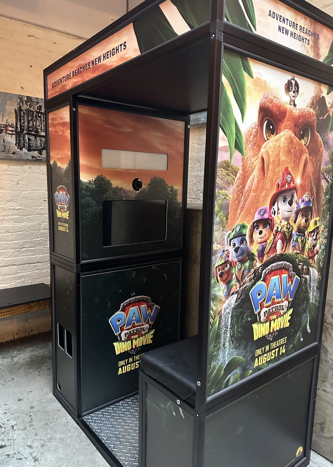 Promotional PAW Patrol: Dino Movie display booth with large dinosaur artwork and character images, featuring a built-in screen and front slot.